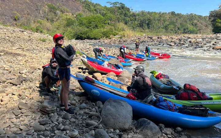 a group of watercraft rest on shore while a person in the foreground carries gear